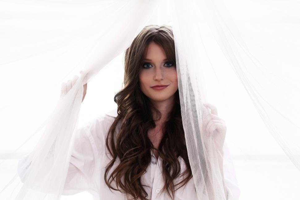 Free Image of Woman is standing by the window playing with curtains 