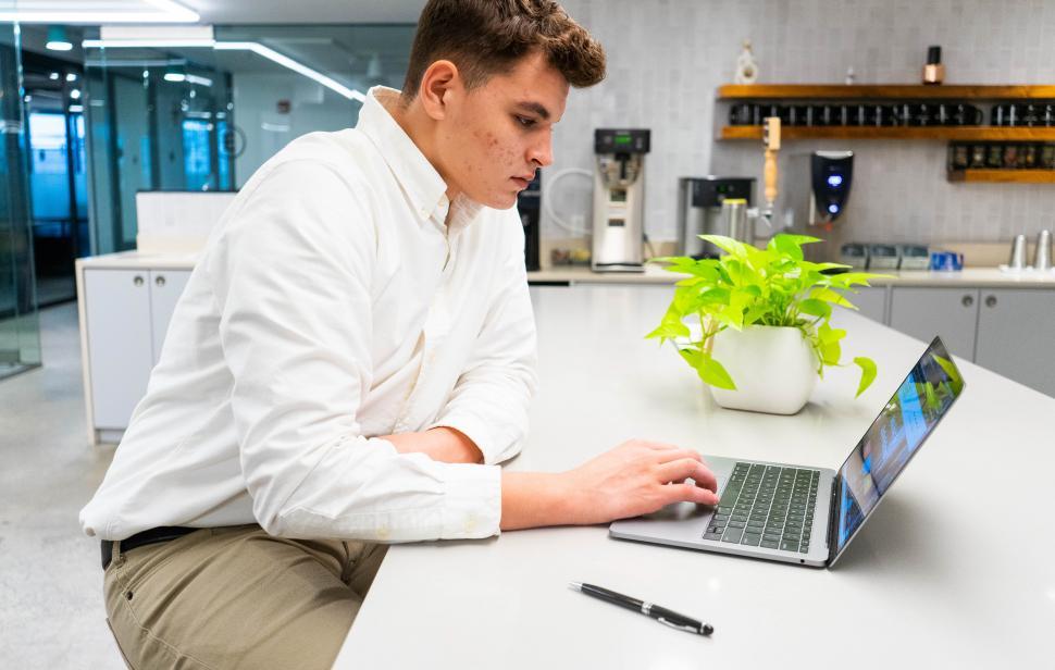 Free Image of Young man working on laptop with plant on table in kitchen area 