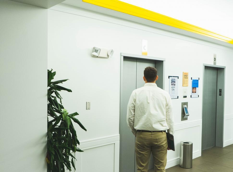 Free Image of Young man holding a laptop as waiting for the elevator in office 
