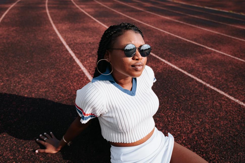 Free Image of Young female athlete in hoop earrings sitting on running track 