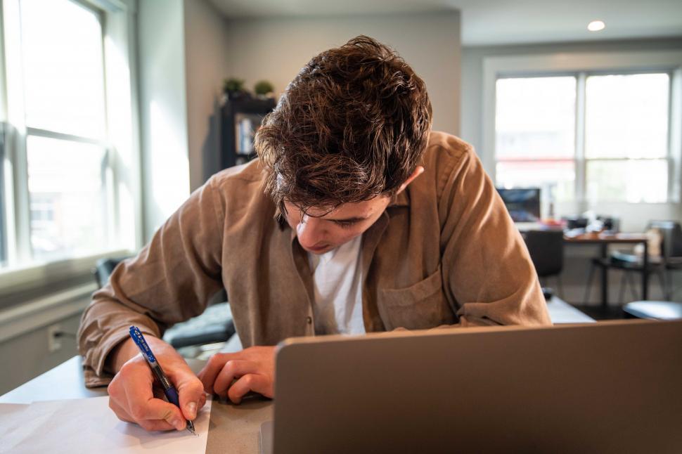 Free Image of Young man taking notes with laptop on table 