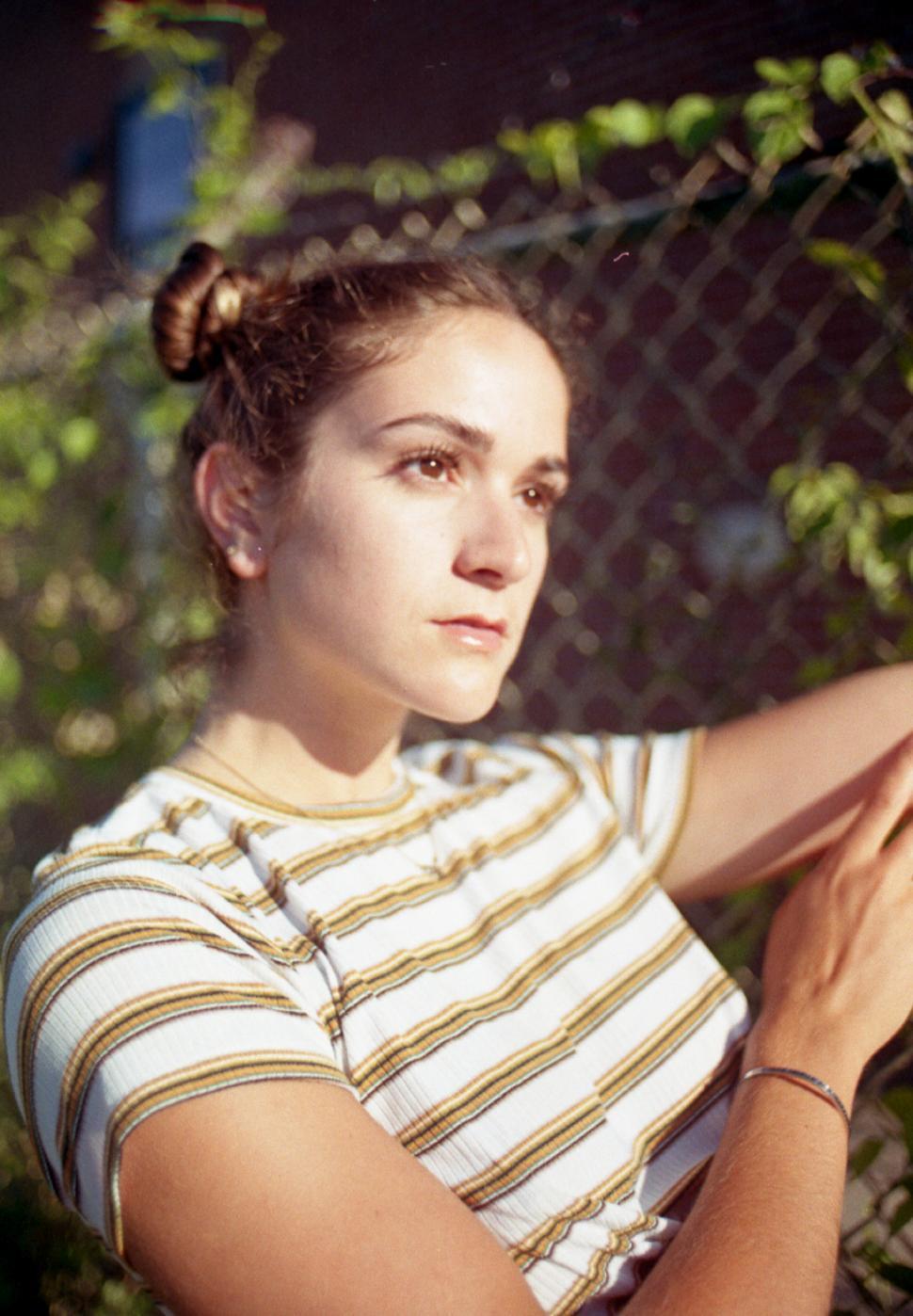 Free Image of Young woman in striped t shirt with fence in the park 
