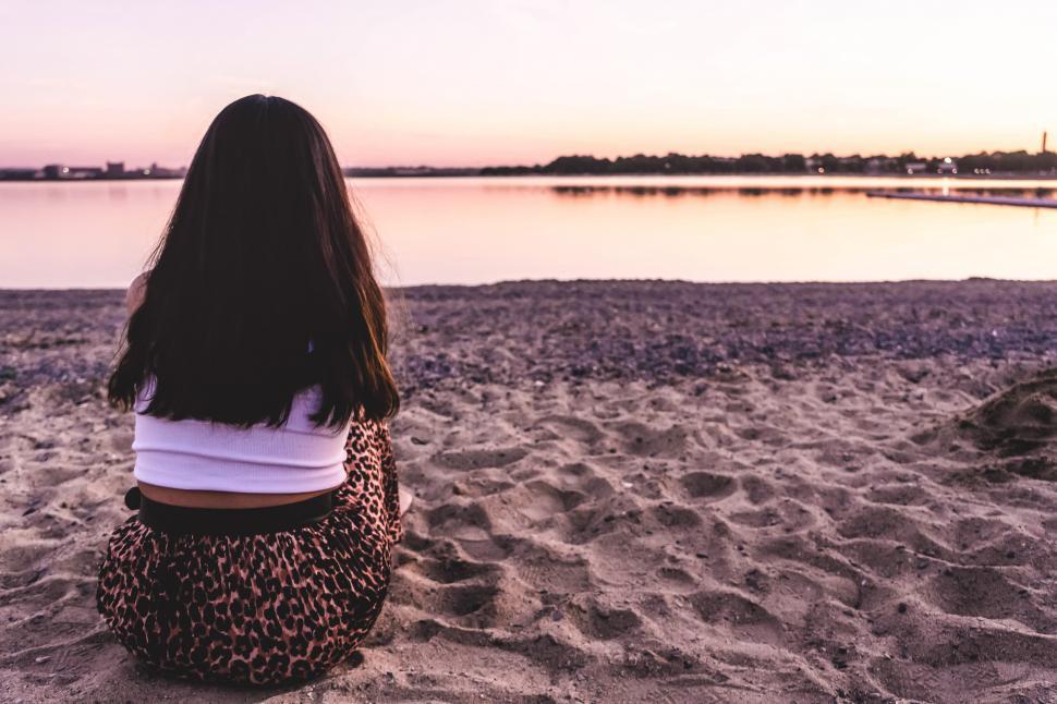 Free Image of Backside view of alone woman in white tank top sitting on beach 