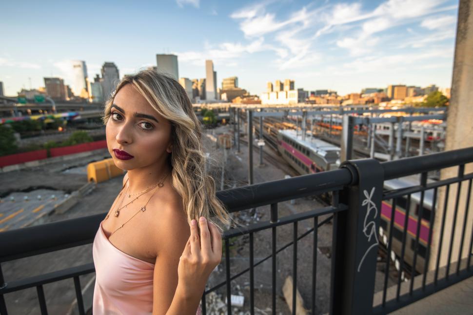 Free Image of Young blonde woman standing on bridge with train and buildings i 