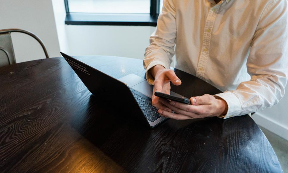 Free Image of Mobile phone in hand with laptop on table 