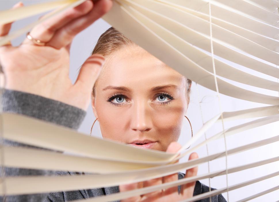Free Image of Woman separates blinds to see through 