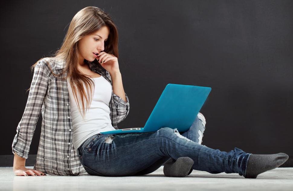 Free Image of Young woman sitting on the floor, looking at her laptop 
