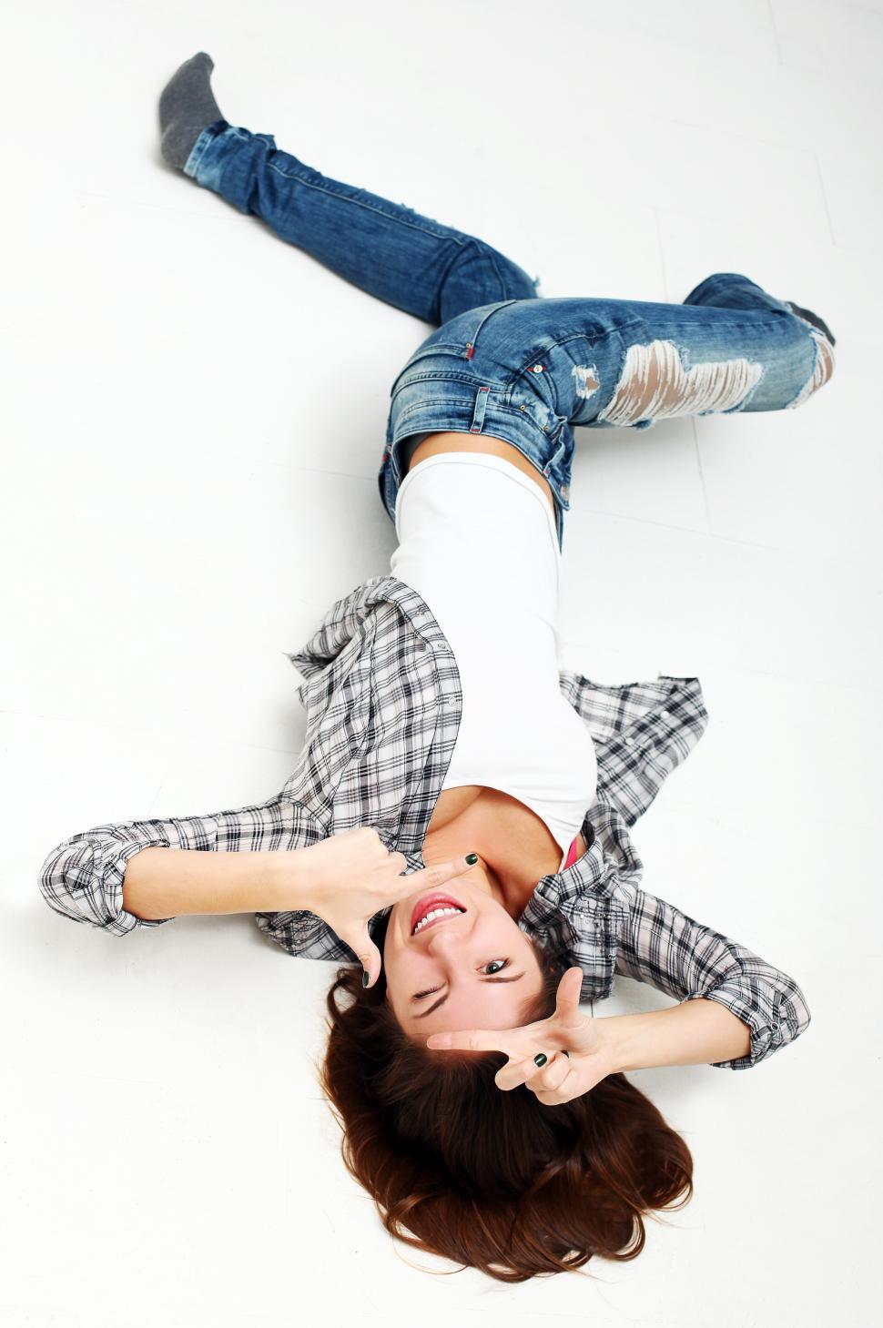Free Image of Young woman sprawled on the floor making framing fingers at the camera 