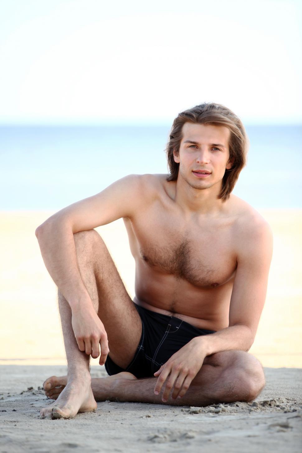 Free Image of Young and handsome guy sitting on the beach 