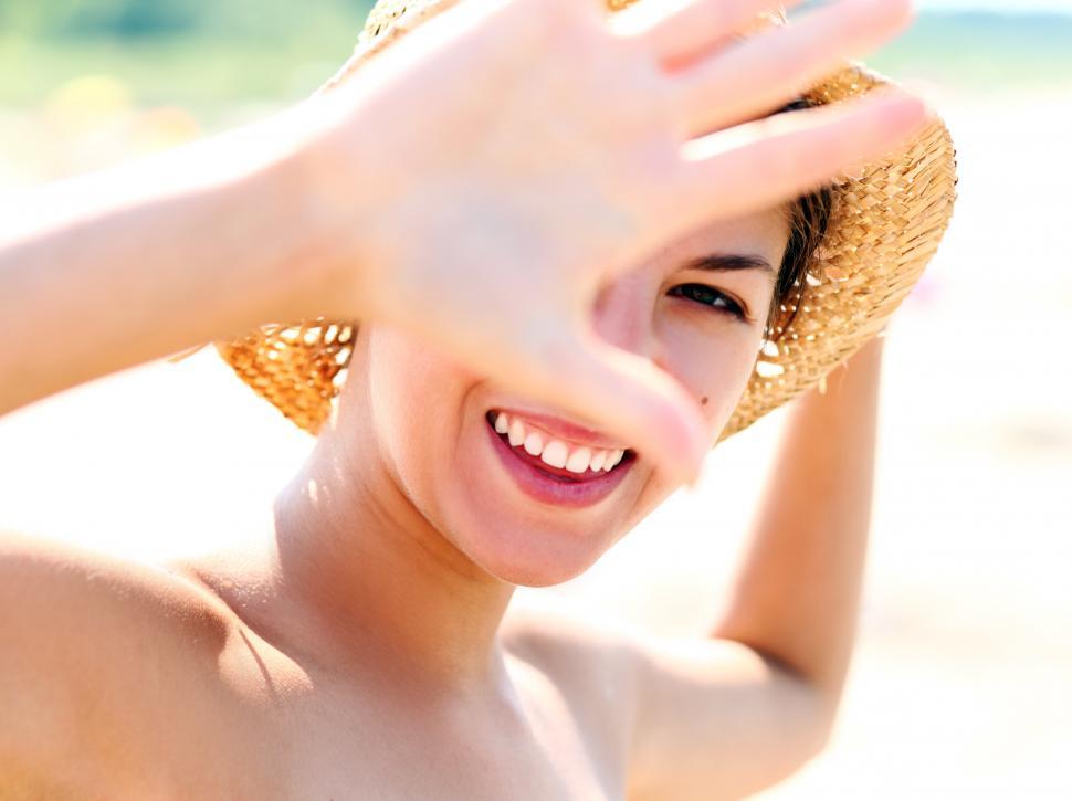 Free Image of Happy woman in straw hat on the beach, shielding her eyes 