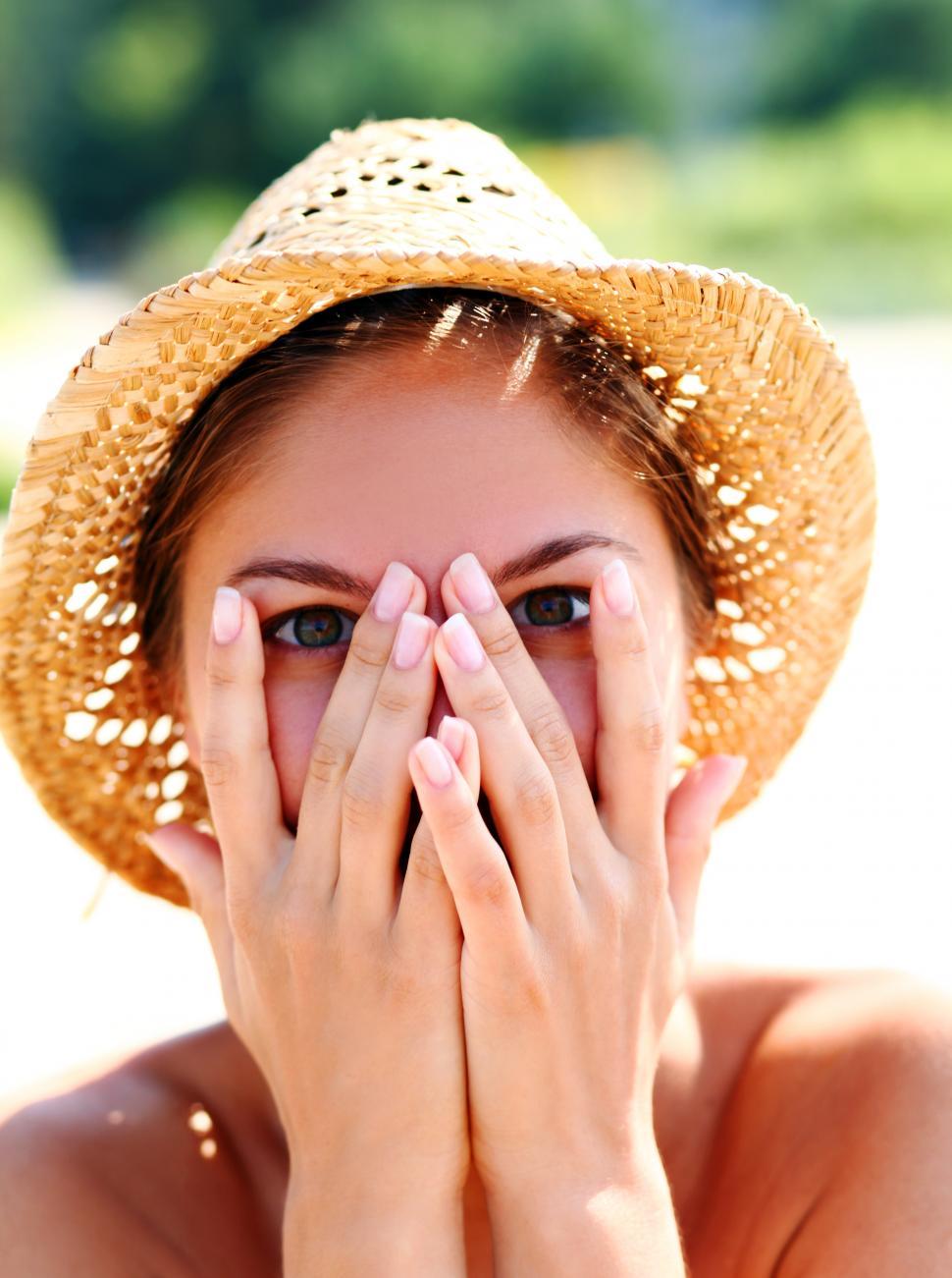 Free Image of Happy woman in straw hat on the beach, hands over her face 