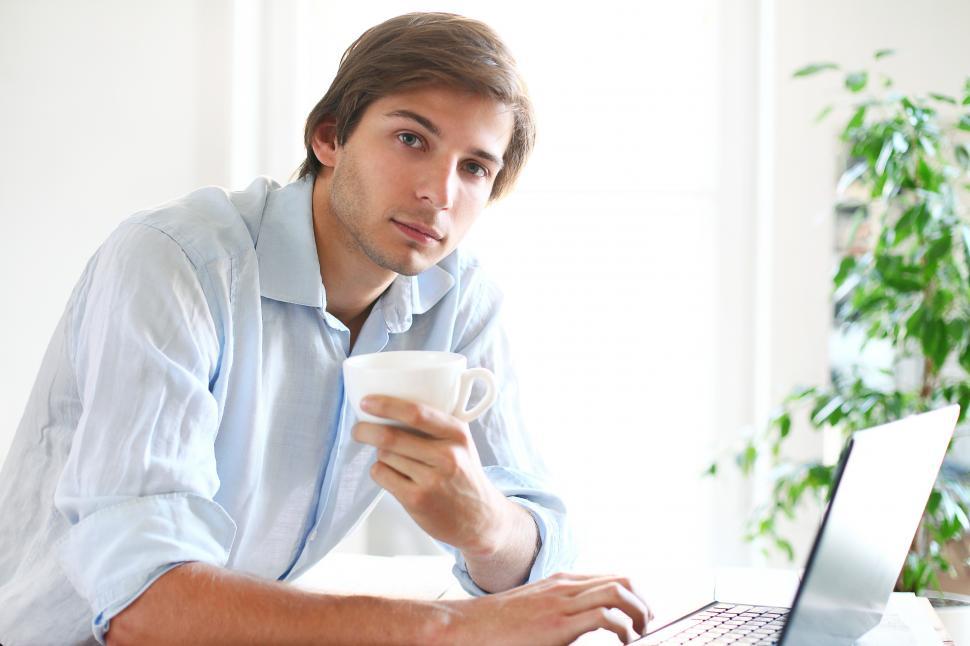 Free Image of Man holds a cup of coffee and looks contemplative 