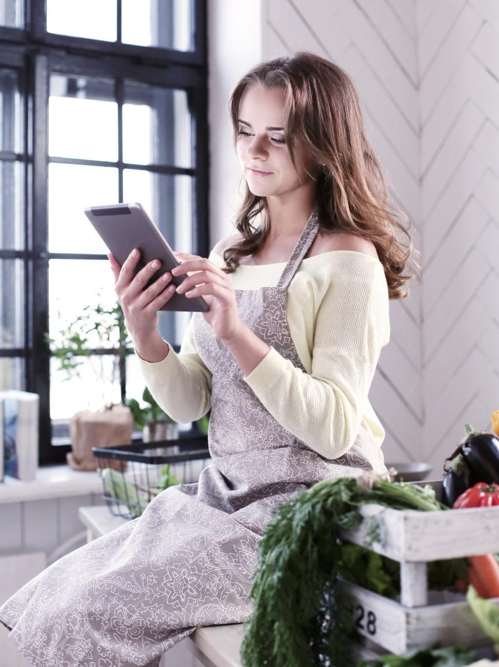 Free Image of Woman looking at tablet device in the kitchen 