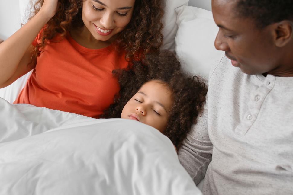 Free Image of Young parents with sleeping girl child in bed 