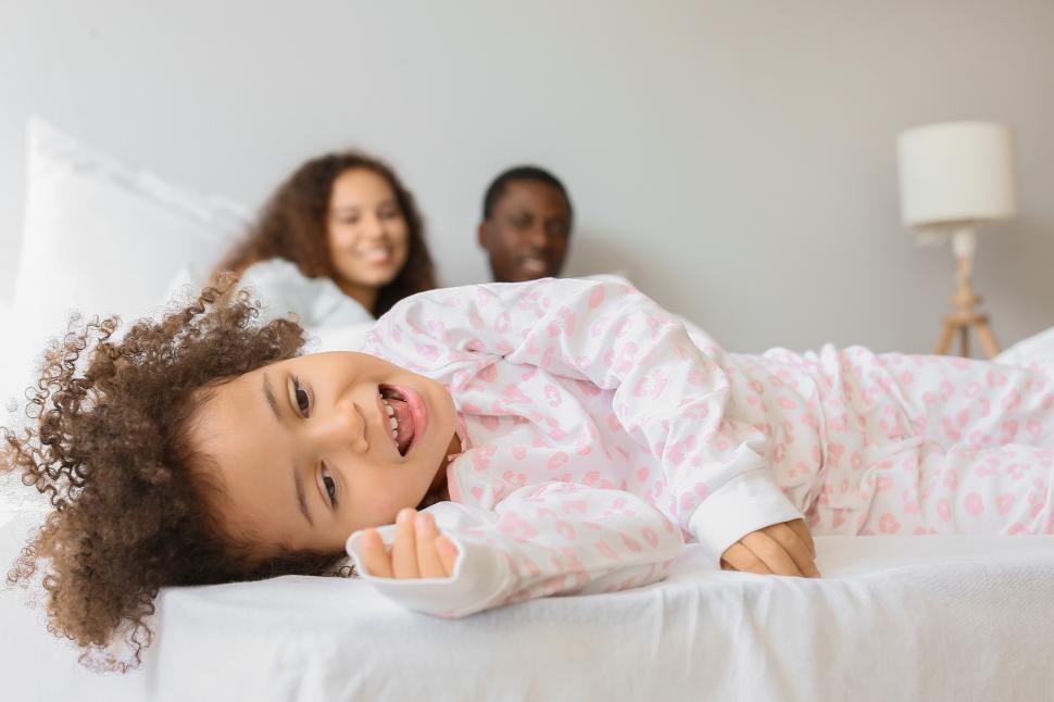Free Image of Smiling little daughter with young mother and father in bed 