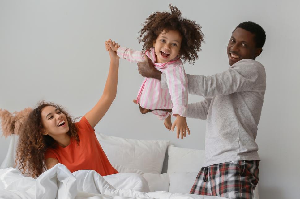 Free Image of Cheerful young mother and father playing with girl child in bed 