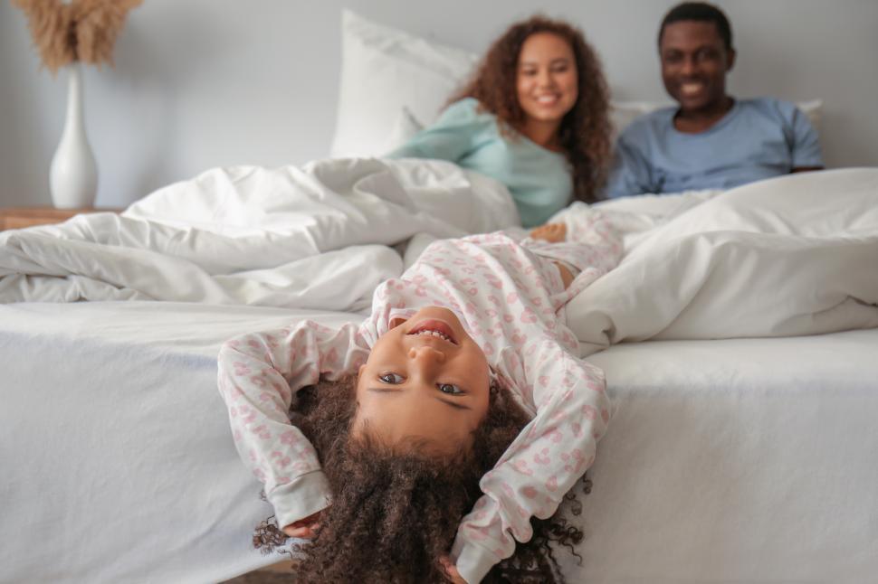 Free Image of Young smiling mother and father with girl child in bed 