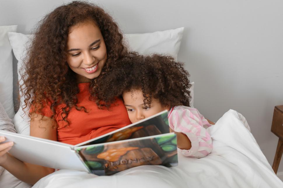 Free Image of Young happy mother reading a book to her daughter in bed 