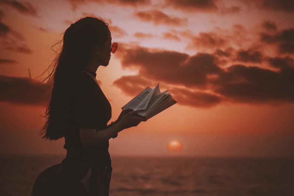 Free Image of Woman with book at the beach during sunset 