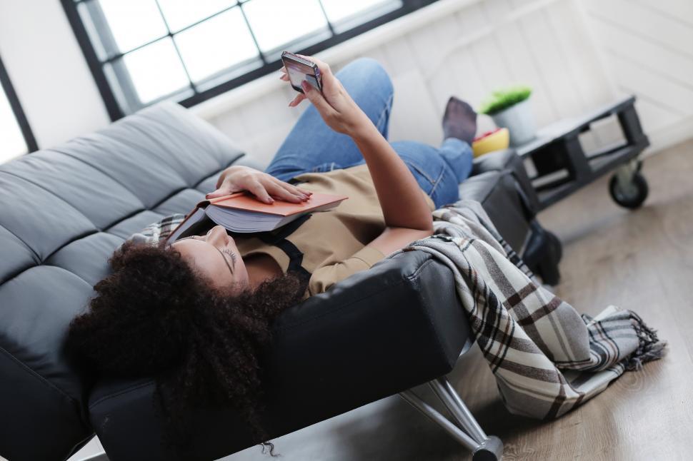Free Image of Woman at home browsing on her phone after reading a book 