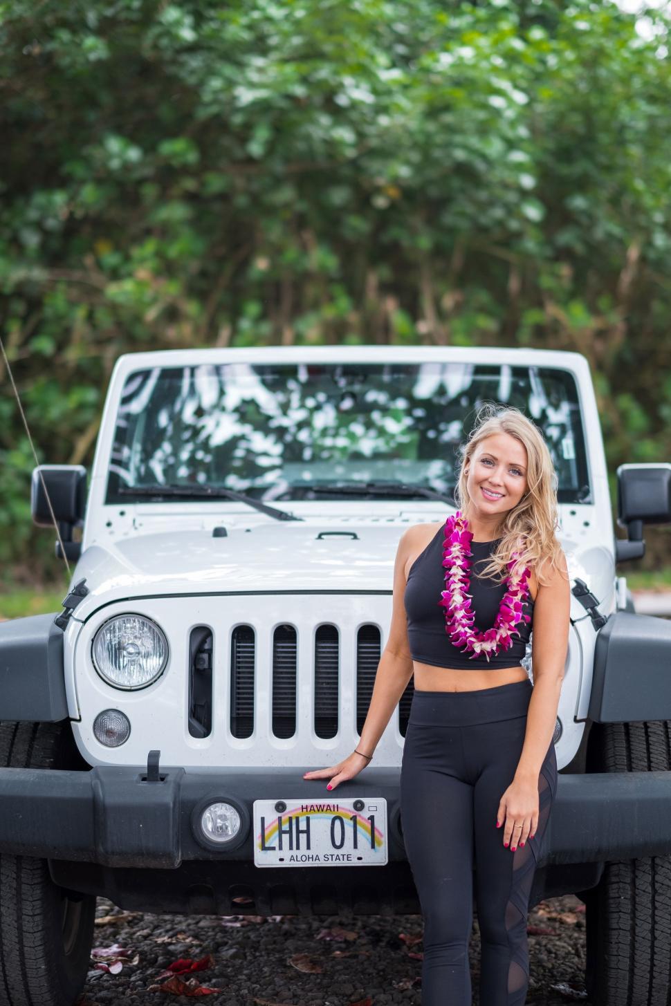 Free Image of Smiling woman with hawaiian flower garland standing with car 