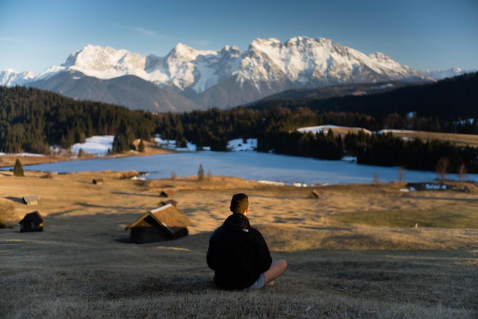 Free Image of Young male sitting and meditating near lake and snow mountains 