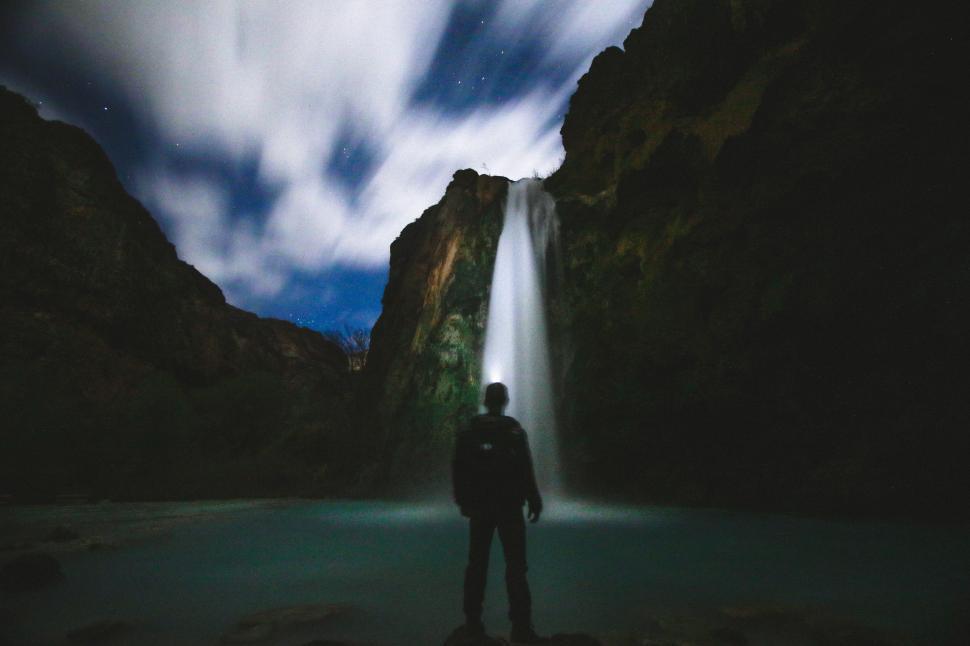 Free Image of Backside view of man and mountain waterfall with night sky 