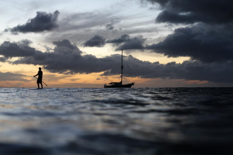 Free Image of Paddle boarder and boat with dramatic sunset sky 