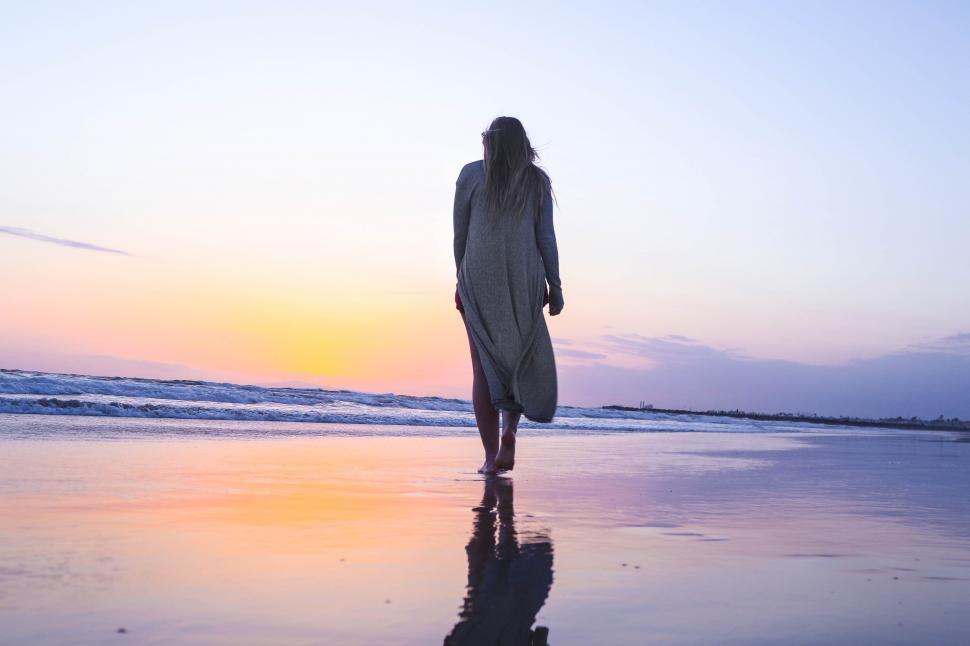 Free Image of Woman walking at the beach with sunset sky and ocean 