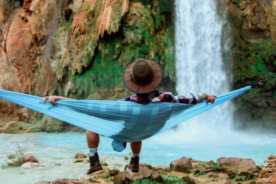Free Image of Man relaxing on hammock with waterfall in forest 
