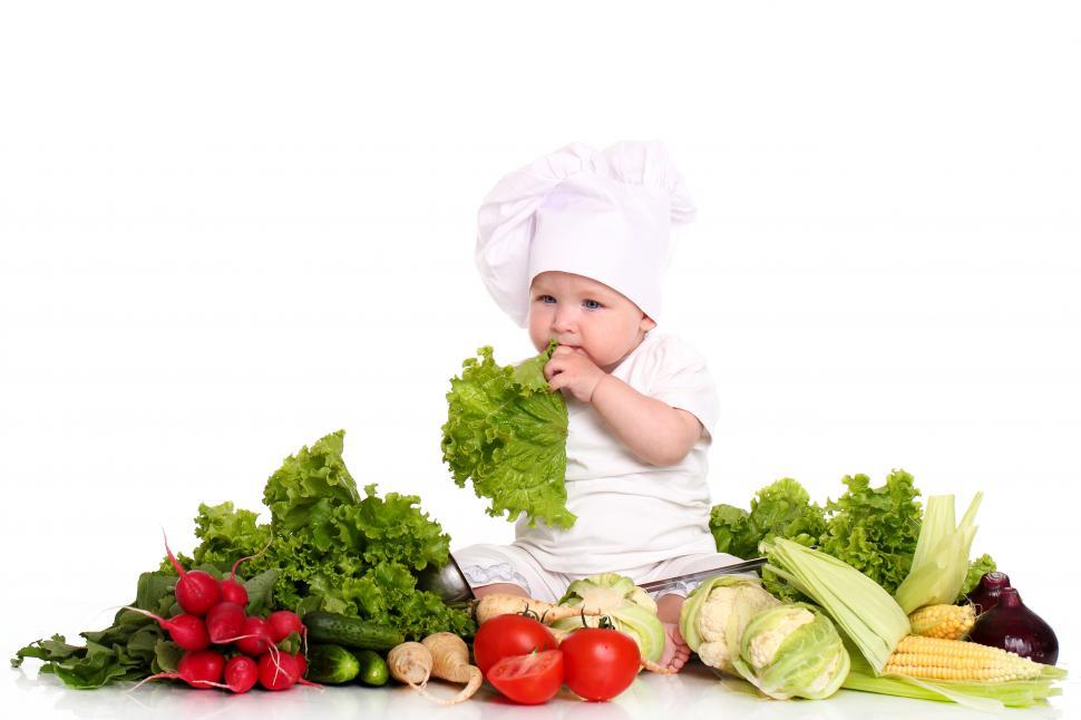 Free Image of Baby dressed as a chef sits among vegetables 