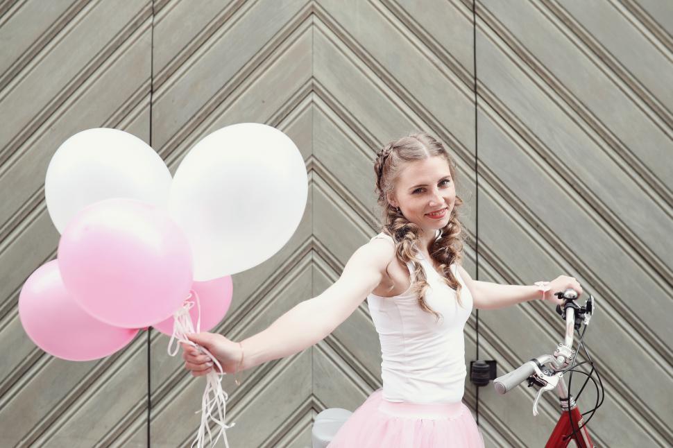 Free Image of Woman with bicycle and pink and white balloons  