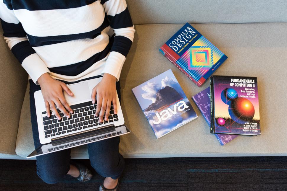 Free Image of Female developer hands on laptop with  books on couch 