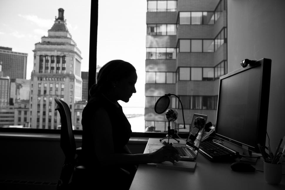 Free Image of Woman using computers in office near window - b&w 