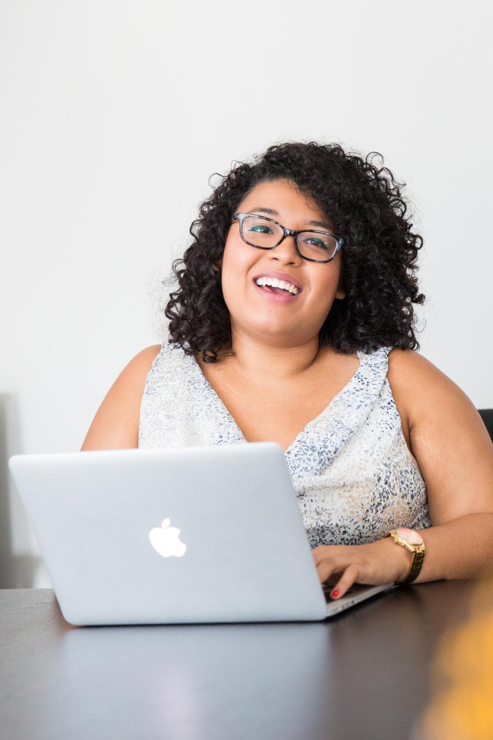 Free Image of Happy woman with curly hair sitting with laptop in office 