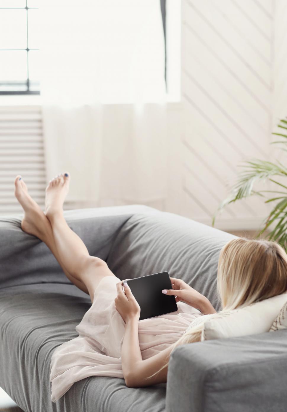 Free Image of Young woman lounges while using tablet device 