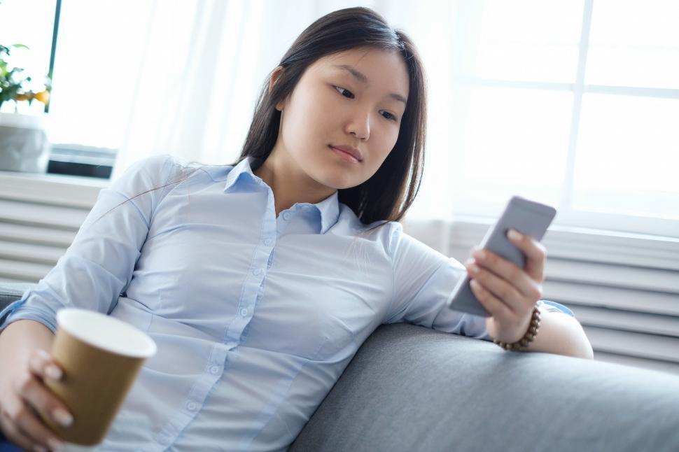 Free Image of Woman is busy with her phone and a cup of coffee 