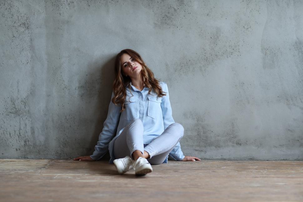 Free Image of Woman sitting against a large concrete wall 