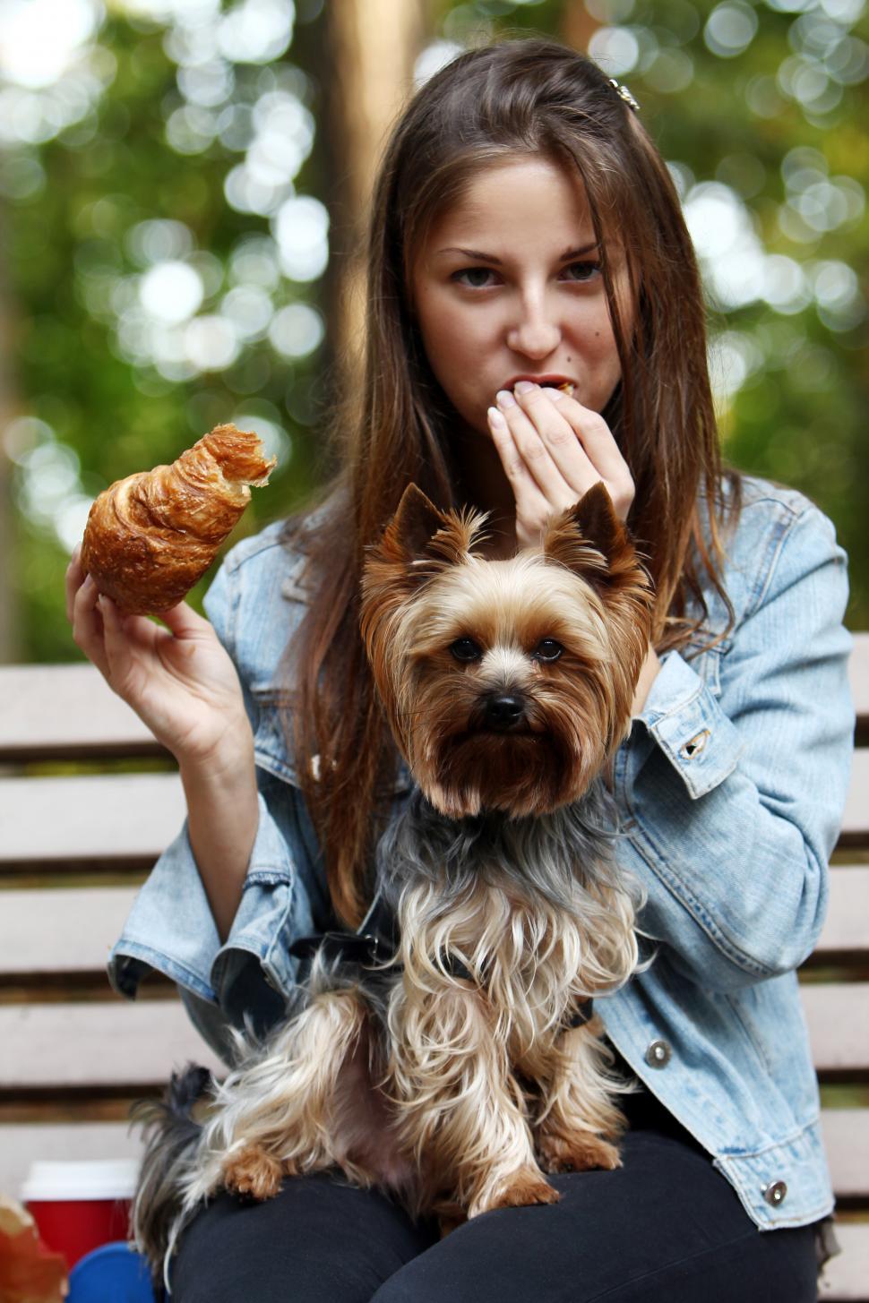 Free Image of Woman eating croissant while sitting with her dog 