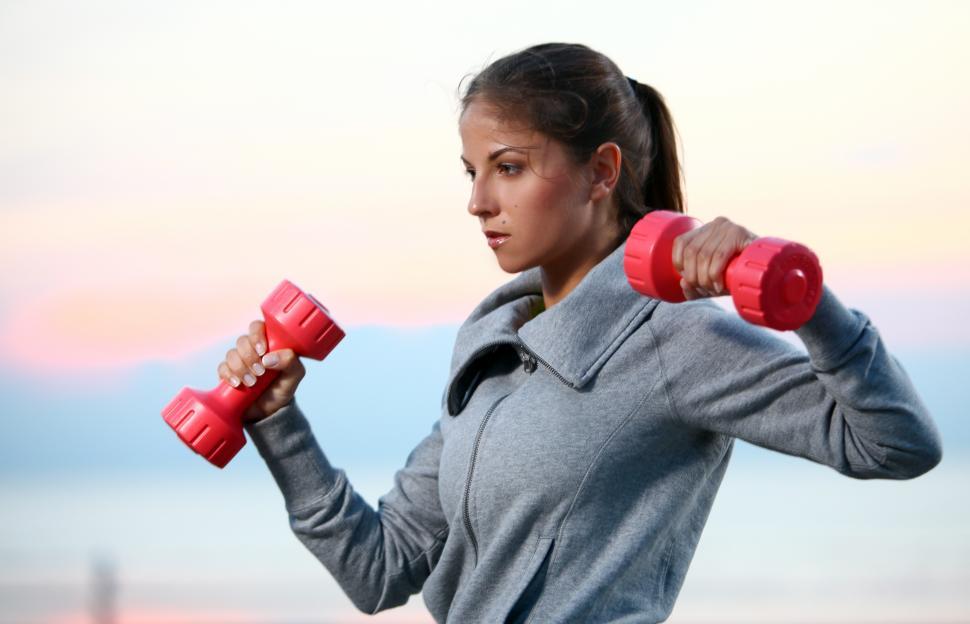 Free Image of Woman in sweats doing exercises with dumbbells on the beach 