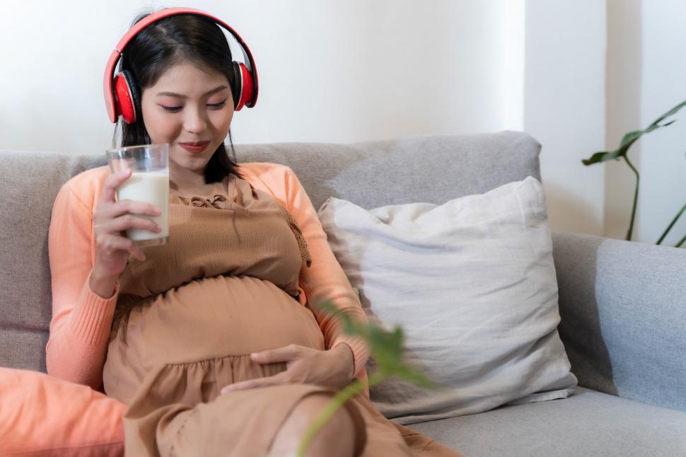 Free Image of Asian happy pregnant woman is sitting on bed listening to music 