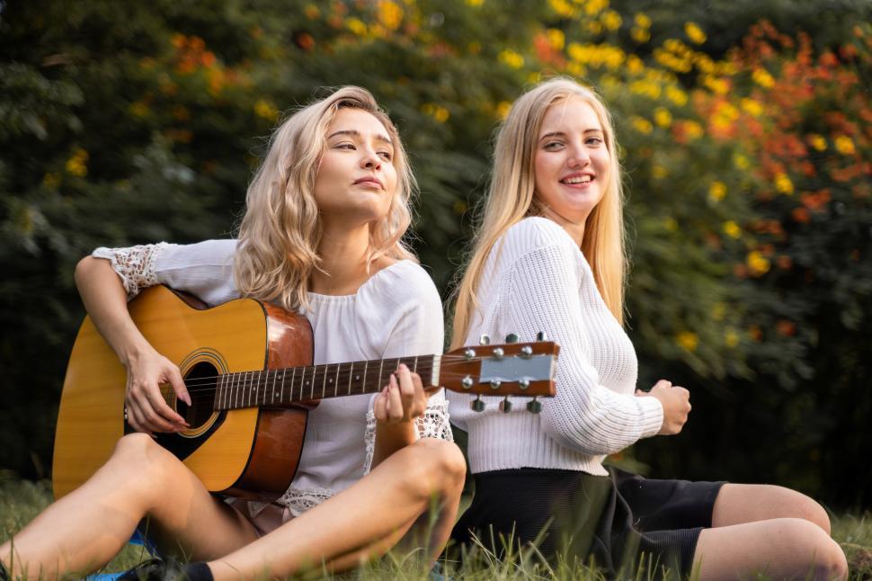Free Image of Portrait of caucasian young women sitting in the park playing guitar 