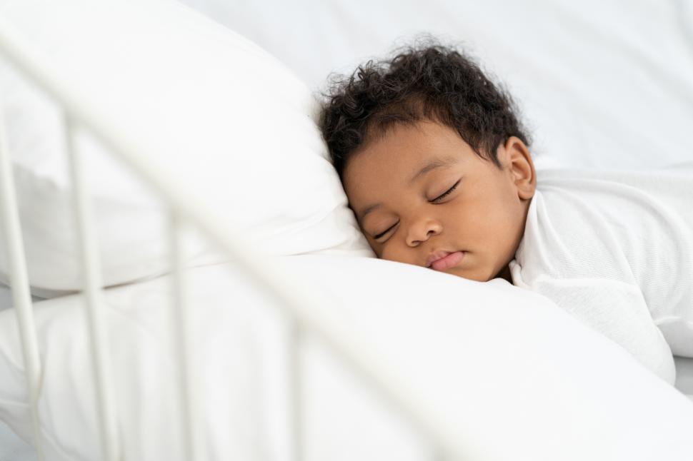 Free Image of baby boy sleeping on a fluffy white mattress 