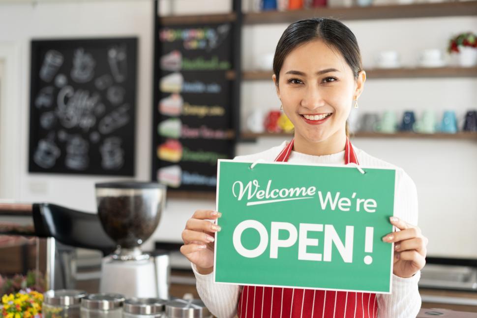 Free Image of Portrait of woman owner standing at her coffee shop holding and Open sign 