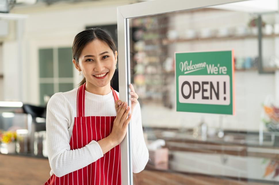 Free Image of Owner standing at her coffee shop door, holding it Open 
