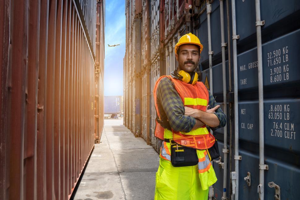 Free Image of Man in helmet and ear protection stands in containers 