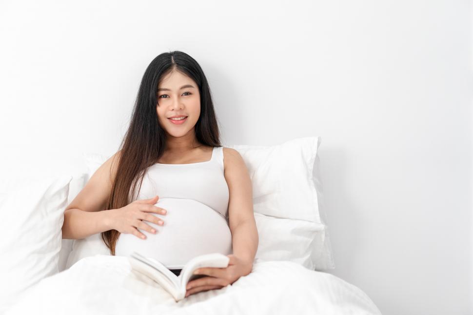 Free Image of Pregnant woman is sitting and reading a book on bed 