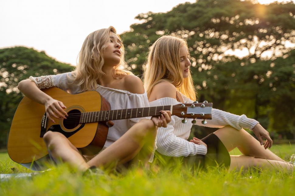 Free Image of two young women friends outdoors playing a guitar 