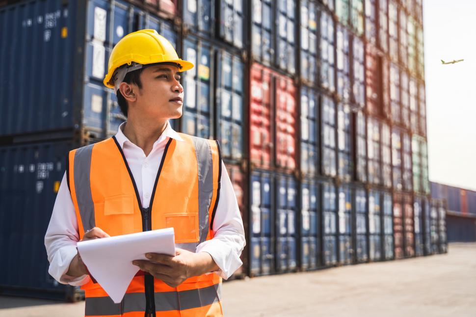 Free Image of A worker wearing a yellow hard hat and directing loading of containers 