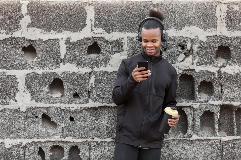 Free Image of Black man with drink using smartphone near wall 